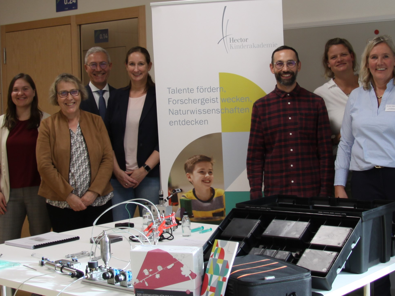 Auftakt für die Hector Akademie in Neuhausen: Eine Gruppe von Menschen steht lächelnd hinter einem Tisch mit technischem Equipment; im Hintergrund ist ein Banner, auf dem "Hector" zu erkennen ist.